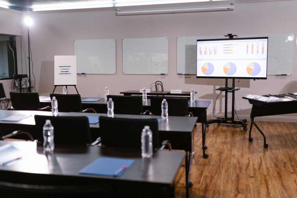 pexels-photo-7648467-7648467 Modern conference room with projector, graphs, chairs, and bottled water setup for presentation.